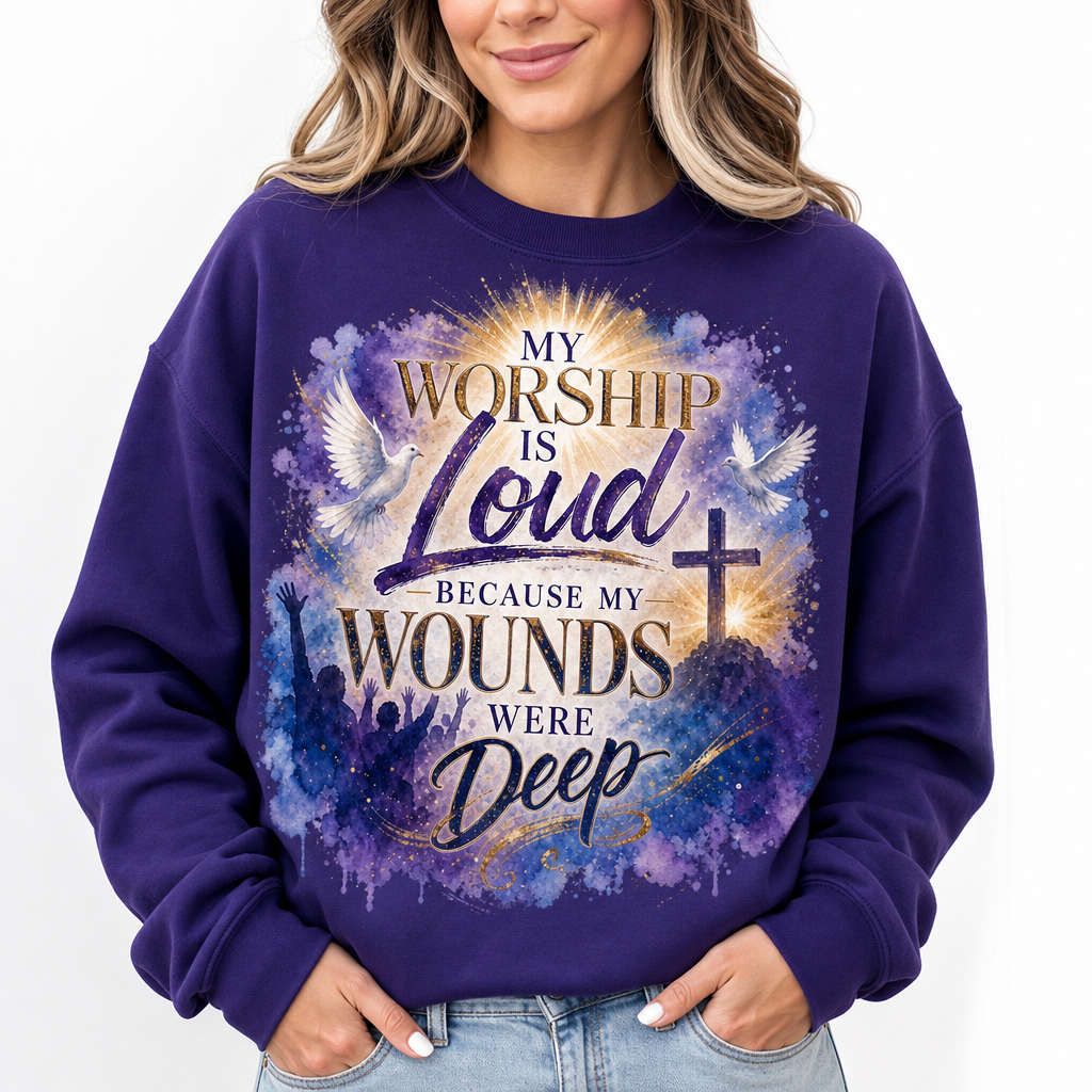 A woman wearing a purple crewneck sweatshirt with a graphic print that reads 'MY WORSHIP IS Loud BECAUSE MY WOUNDS WERE Deep' in gold and white lettering over a blue, purple, and gold watercolor design with a cross and doves.